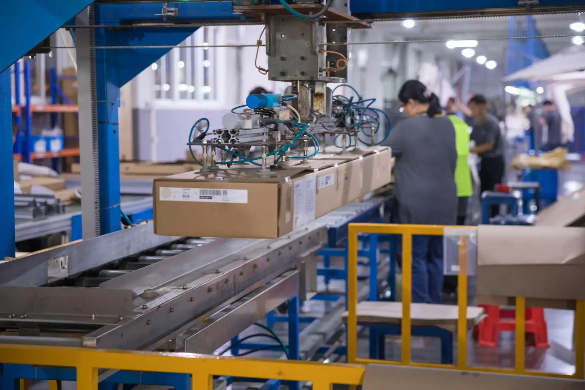 A robotic arm with pneumatic suction cups lifts a perfectly packed product box from a roller conveyor on the automated packaging line, ensuring efficiency and precision.