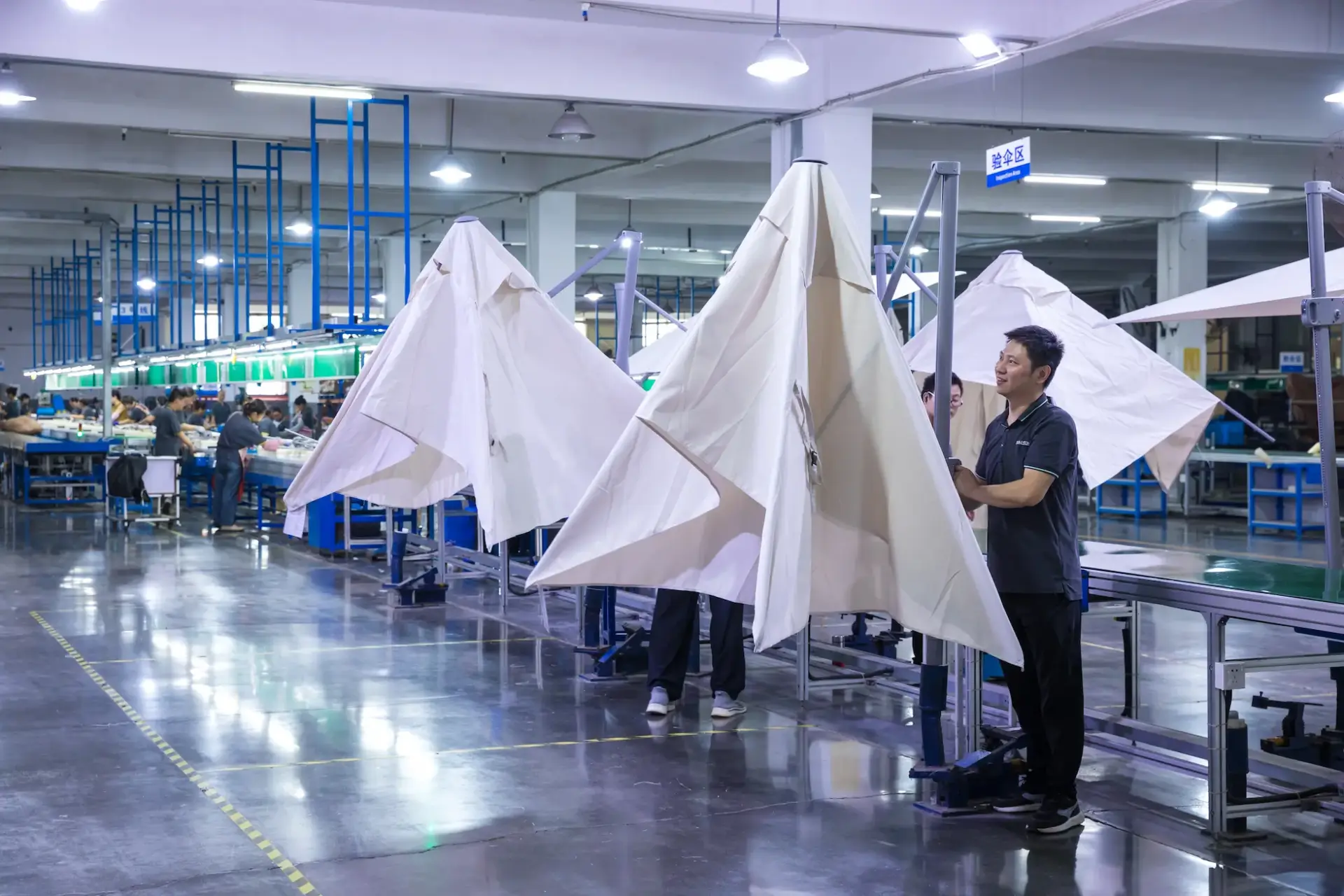 A factory technician inspects large, nearly-assembled umbrellas in the dedicated quality inspection area of the bustling production line.
