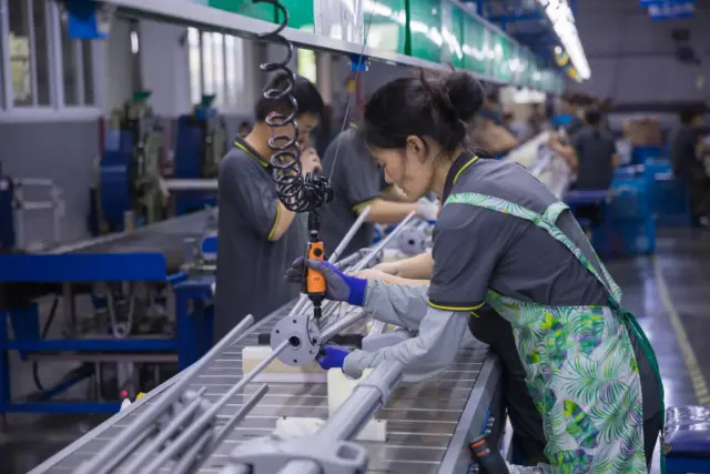 A Tempo Manufacturing worker precisely assembling metal components for an outdoor umbrella frame on a clean, well-lit production line.