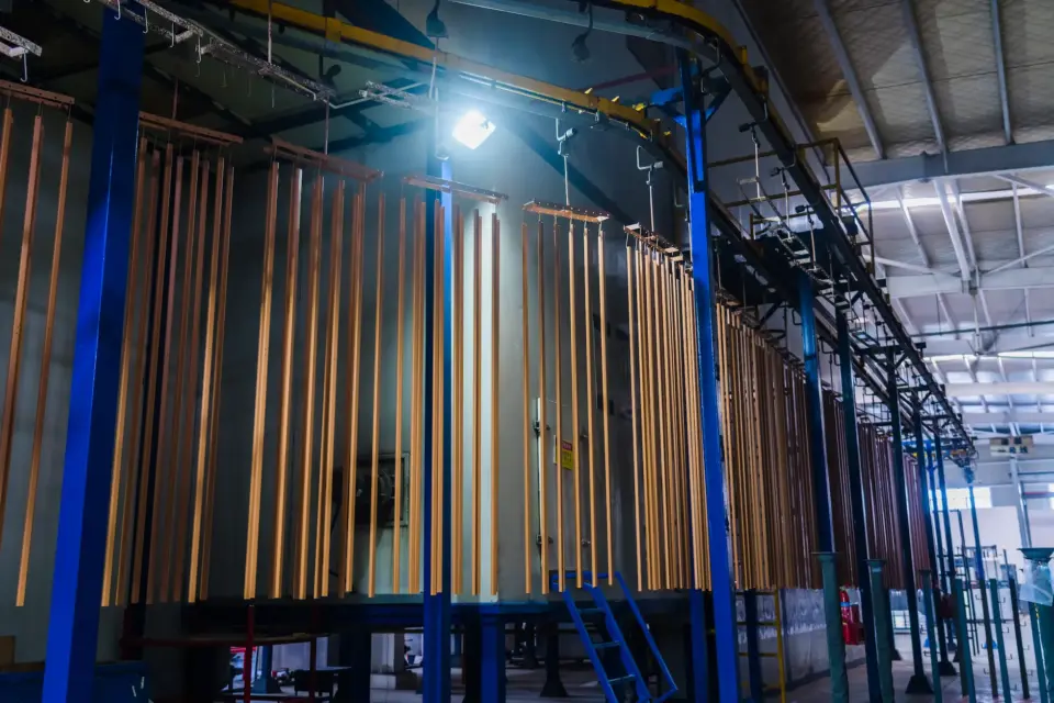Rows of copper-toned metal components hang from the automated overhead conveyor after undergoing a multi-stage surface treatment and coating process.