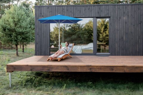 Tempo Frappe square umbrella shown in an outdoor setting, woman relaxing underneath.