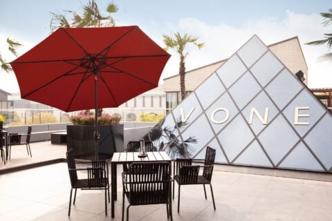 Tempo Sunflower umbrella in red, set in an outdoor patio environment.